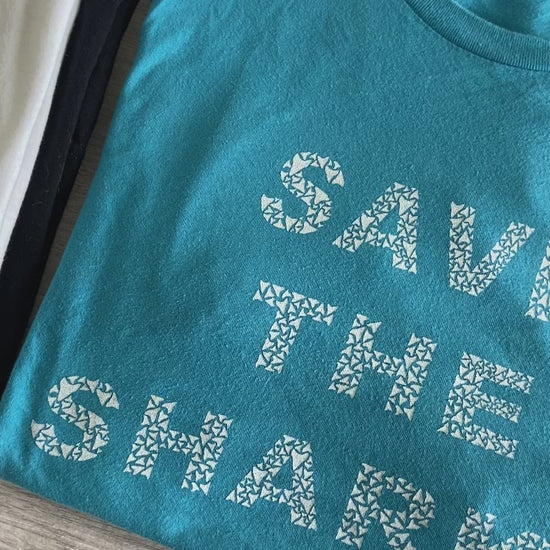 Close up of aqua Save The Sharks Short-Sleeve Unisex T-Shirt reads "Save The Sharks." - Connected Clothing Company - Ethically and Sustainably Made - 10% donated to Oceana shark conservation