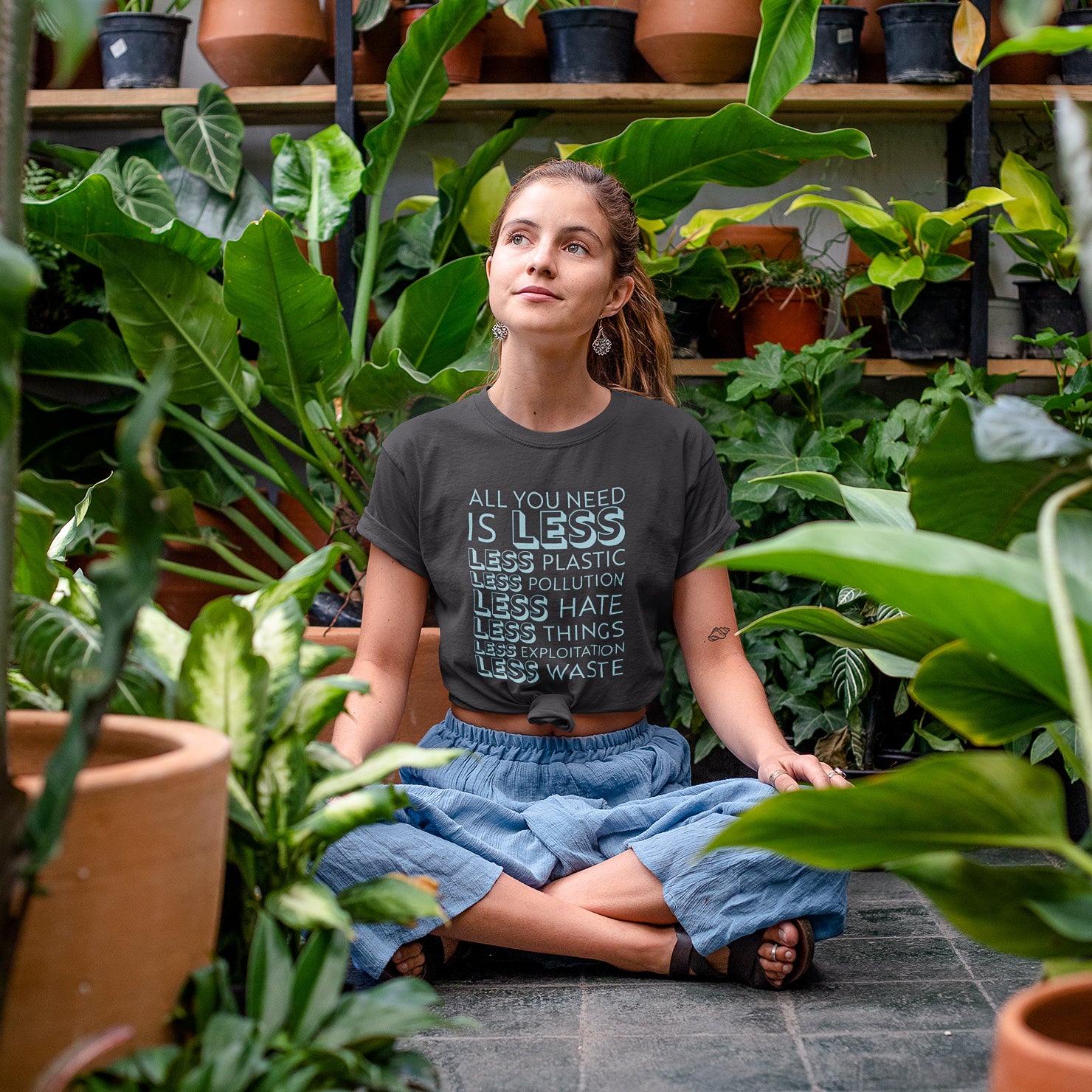 girl in greenhouse surrounded by plants wearing gray Connected Clothing Company "All You Need Is Less" shirt - Connected Clothing Company donated 10% of profits to non-profit organizations - ethically and sustainably made clothing