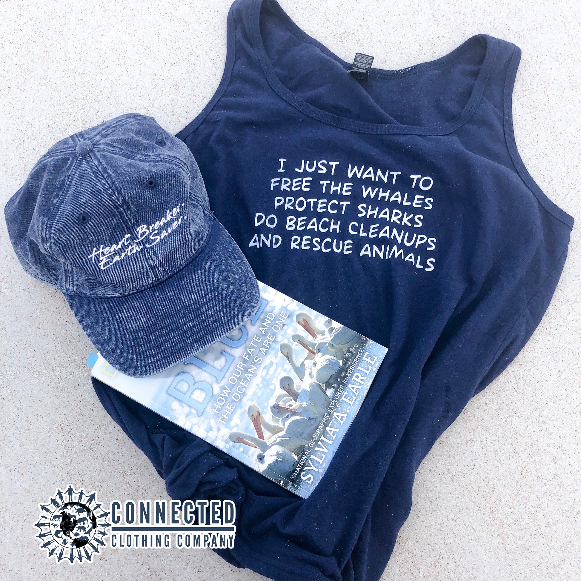 Navy Blue I Just Want To Save The World Women's Relaxed Tank Top on the beach sand with Heart Breaker Earth Saver Cotton Cap and Mission Blue book. - Connected Clothing Company - Ethically and Sustainably Made - 10% donated to Mission Blue ocean conservation